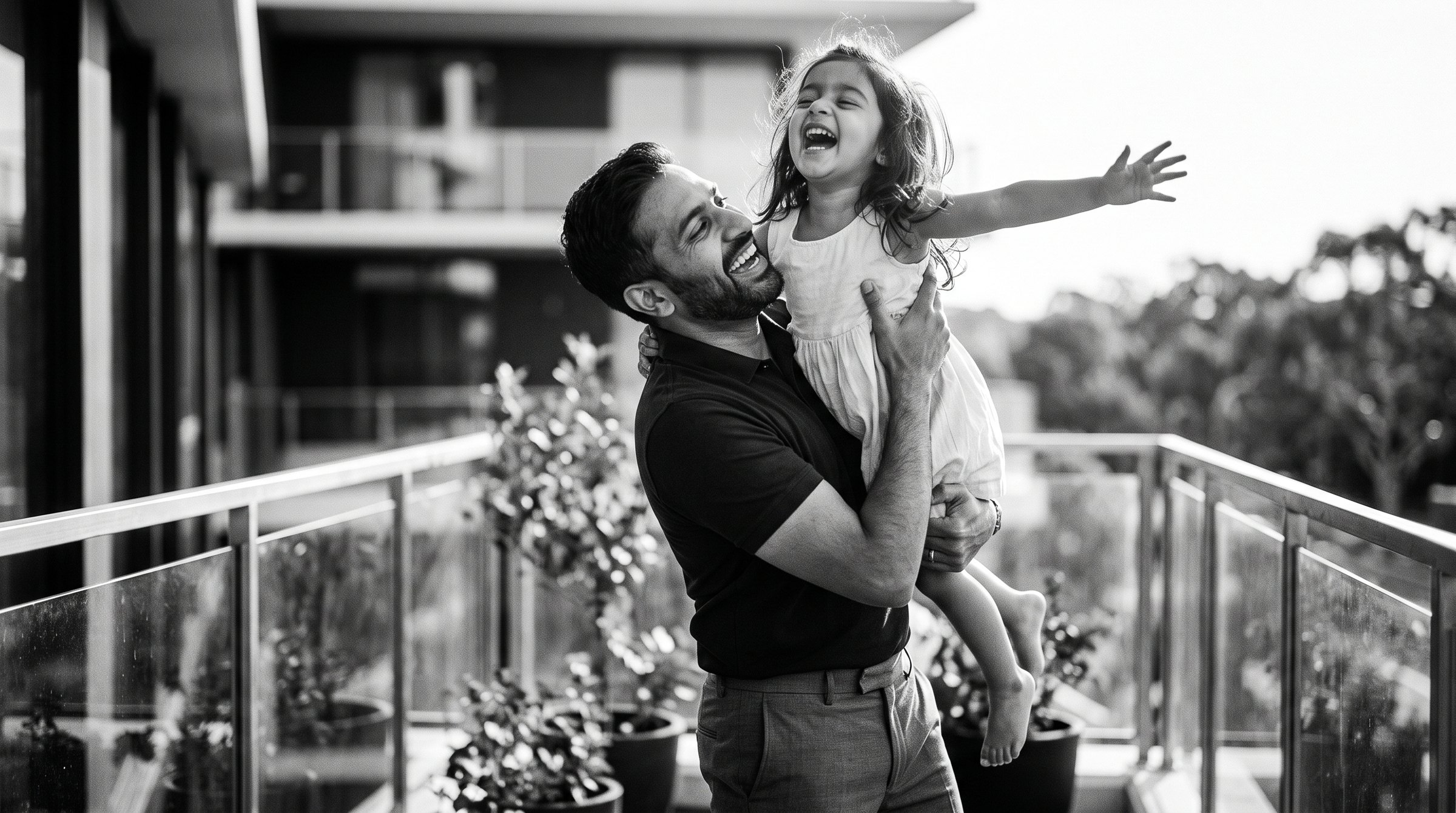 A father lifting his laughing daughter on a sunlit balcony